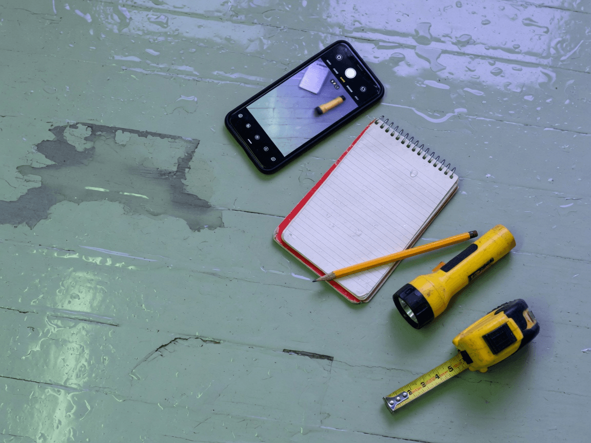 Phone, notebook, flashlight, and tape measure on a damp floor